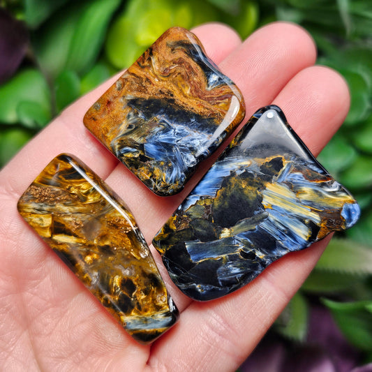 May include: Three blue tiger&#39;s eye gemstone cabochons. The cabochons are various shades of blue, gold, and black. The cabochons are smooth and polished.