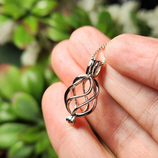 May include: A silver charm necklace with a cage pendant. The cage is made of twisted metal and has a delicate design.