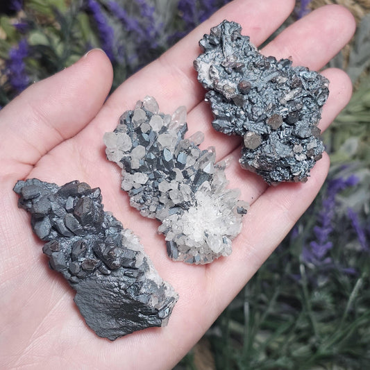 May include: Three specimens of quartz crystals combined with dark gray metallic minerals.  The crystals exhibit a cluster formation, with the clear quartz points interspersed among the darker mineral matrix. The color contrast is striking, creating an interesting visual texture.  These unique mineral specimens would be ideal for collectors or those interested in metaphysical properties.