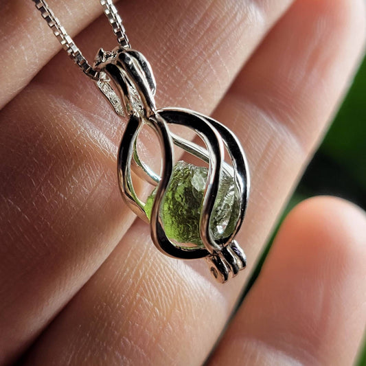 May include: Silver cage pendant necklace with a green olivine gemstone. The intricate, swirling design of the cage securely holds the vibrant, translucent green stone.  The necklace features a delicate silver chain. The olivine gemstone displays subtle variations in its green hue and texture. This elegant piece is perfect for adding a touch of natural beauty and sophistication to any outfit.