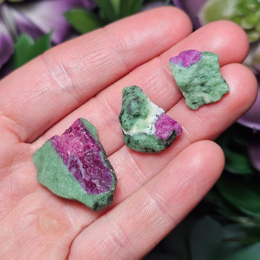 May include: Three green and pink rough gemstones. The gemstones are irregularly shaped and have a mottled green and pink color.