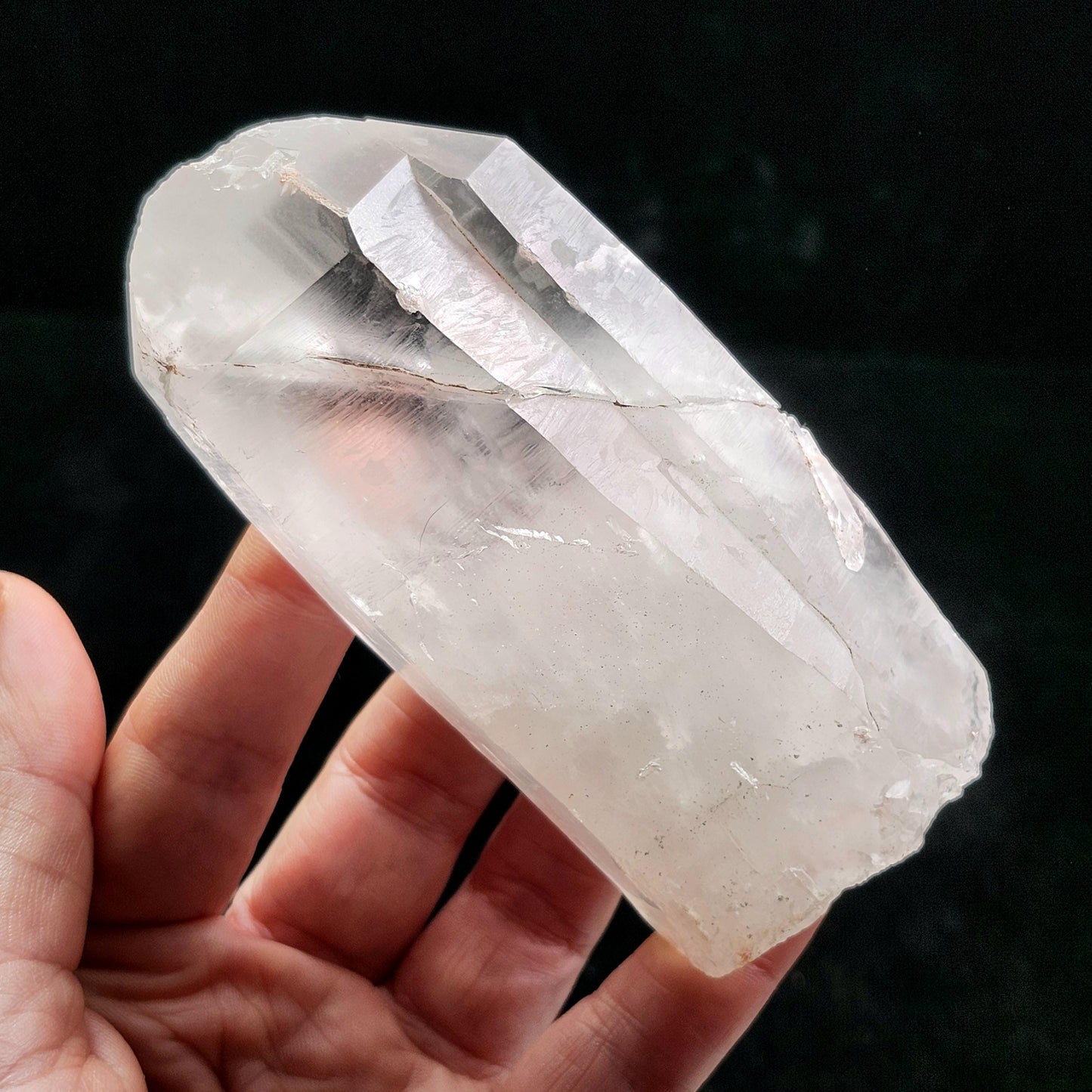 May include: A clear quartz crystal with a faceted, pointed end. The crystal is held in a hand, showcasing its translucent quality and natural, rough texture. The crystal's color is a pale, milky white.