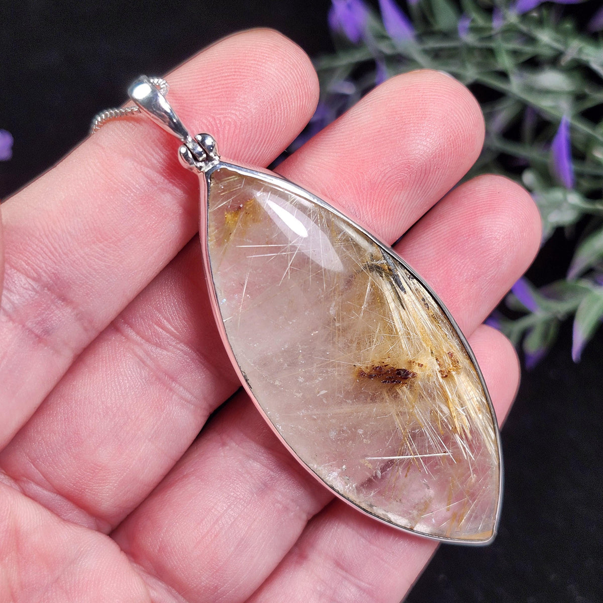 May include: A clear, elongated pendant with a silver-colored metal frame. The pendant contains golden, needle-like inclusions within the transparent stone. The pendant hangs from a delicate silver chain, showcasing a natural gemstone.