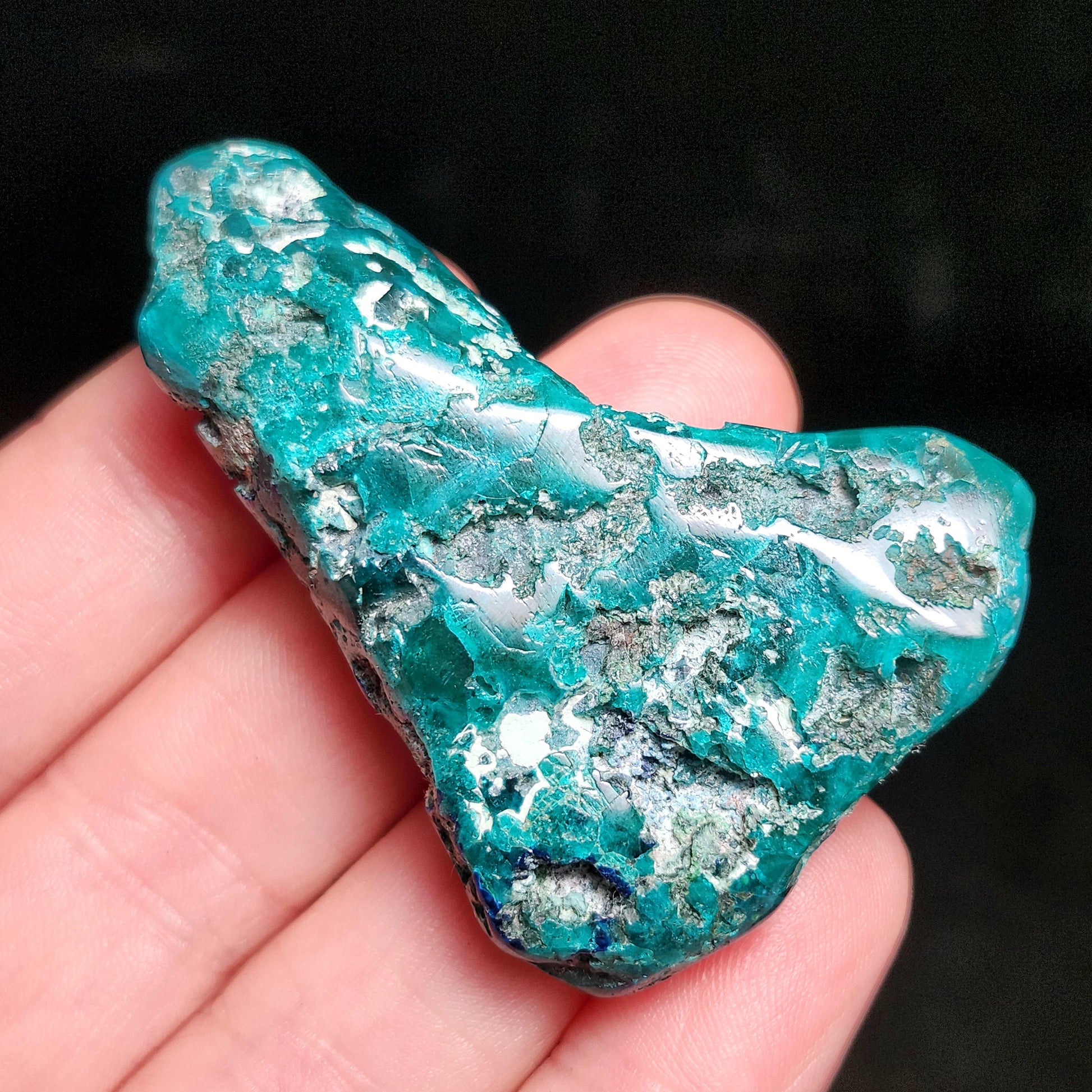 May include: A vibrant, irregularly shaped teal-colored mineral specimen with a metallic sheen. The stone has a rough, textured surface with areas of silver and dark green. The overall appearance is natural and raw, showcasing the mineral's unique crystalline structure.