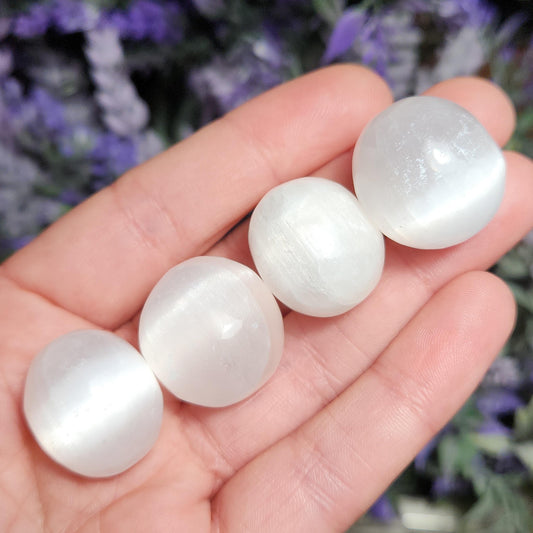 May include: Four smooth, white selenite spheres of varying sizes, displayed on a hand. The spheres have a subtle shimmer and a polished, rounded surface.